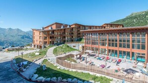 Un hotel con varias plantas, zona de piscina al aire libre y montañas al fondo.