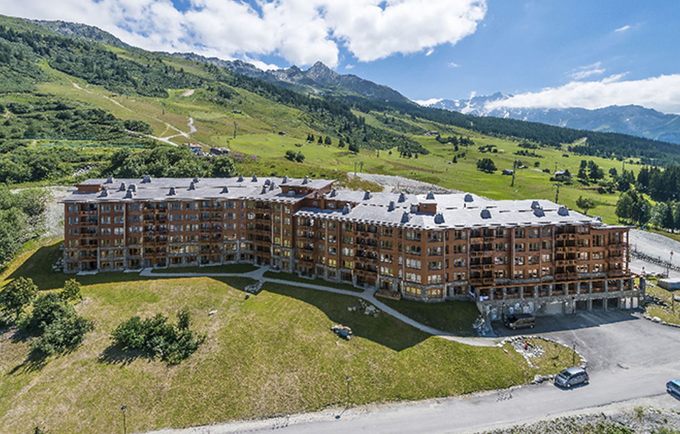 A multi-story hotel with a central courtyard, surrounded by lush green hills and mountains.