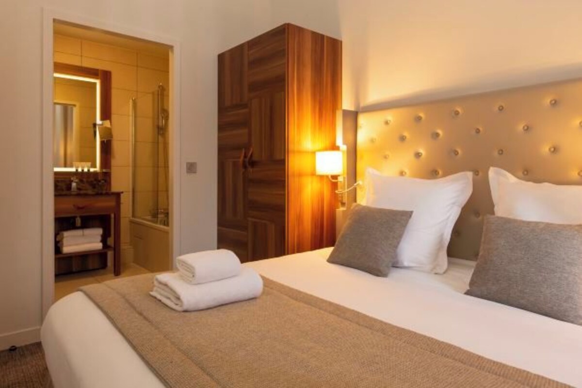 Una habitación de hotel con cama, un armario de madera, baño con ducha y mesita de noche con lámpara.