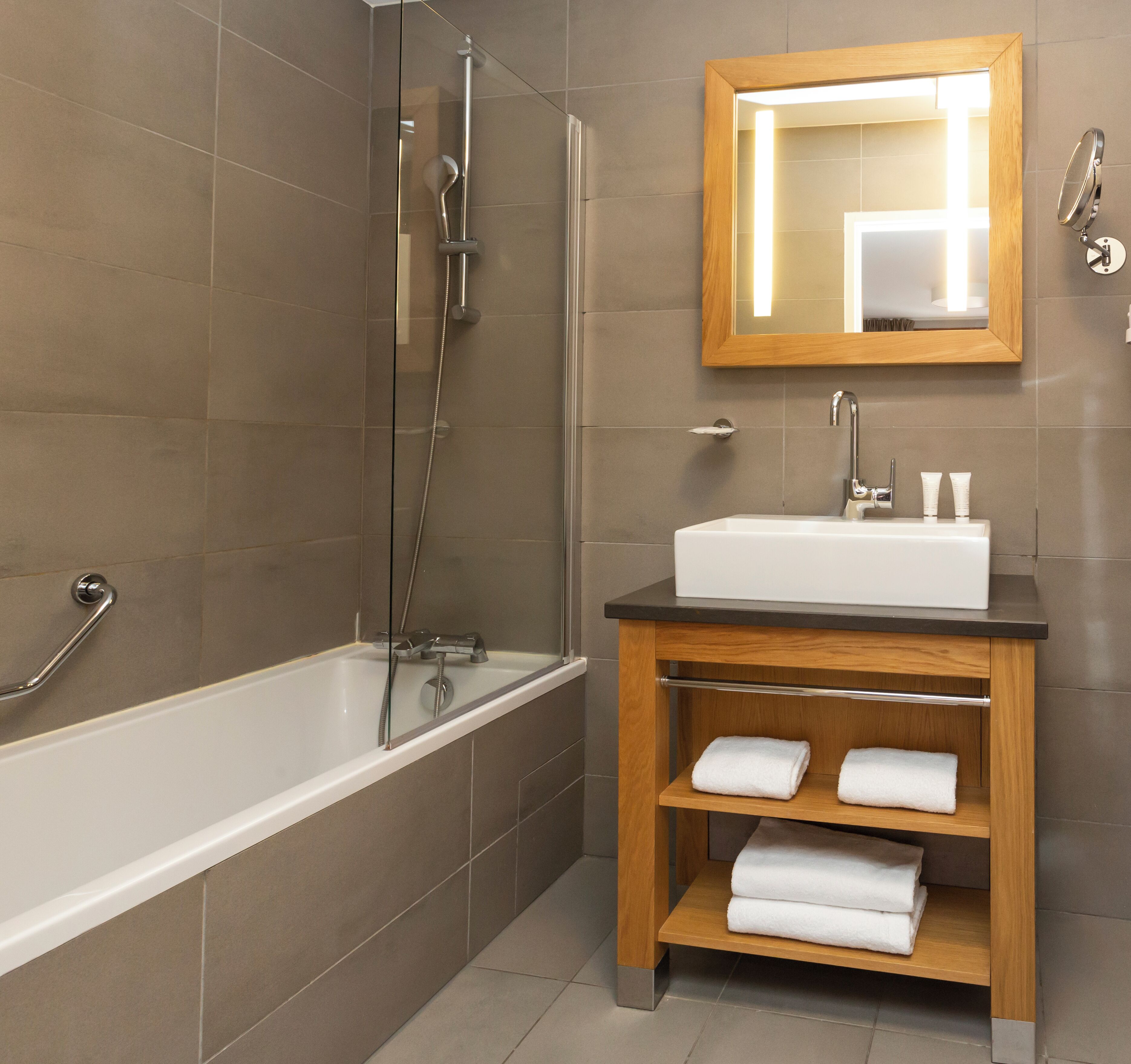 A modern bathroom with a bathtub, a sink with a mirror above it, and a shelf with towels.