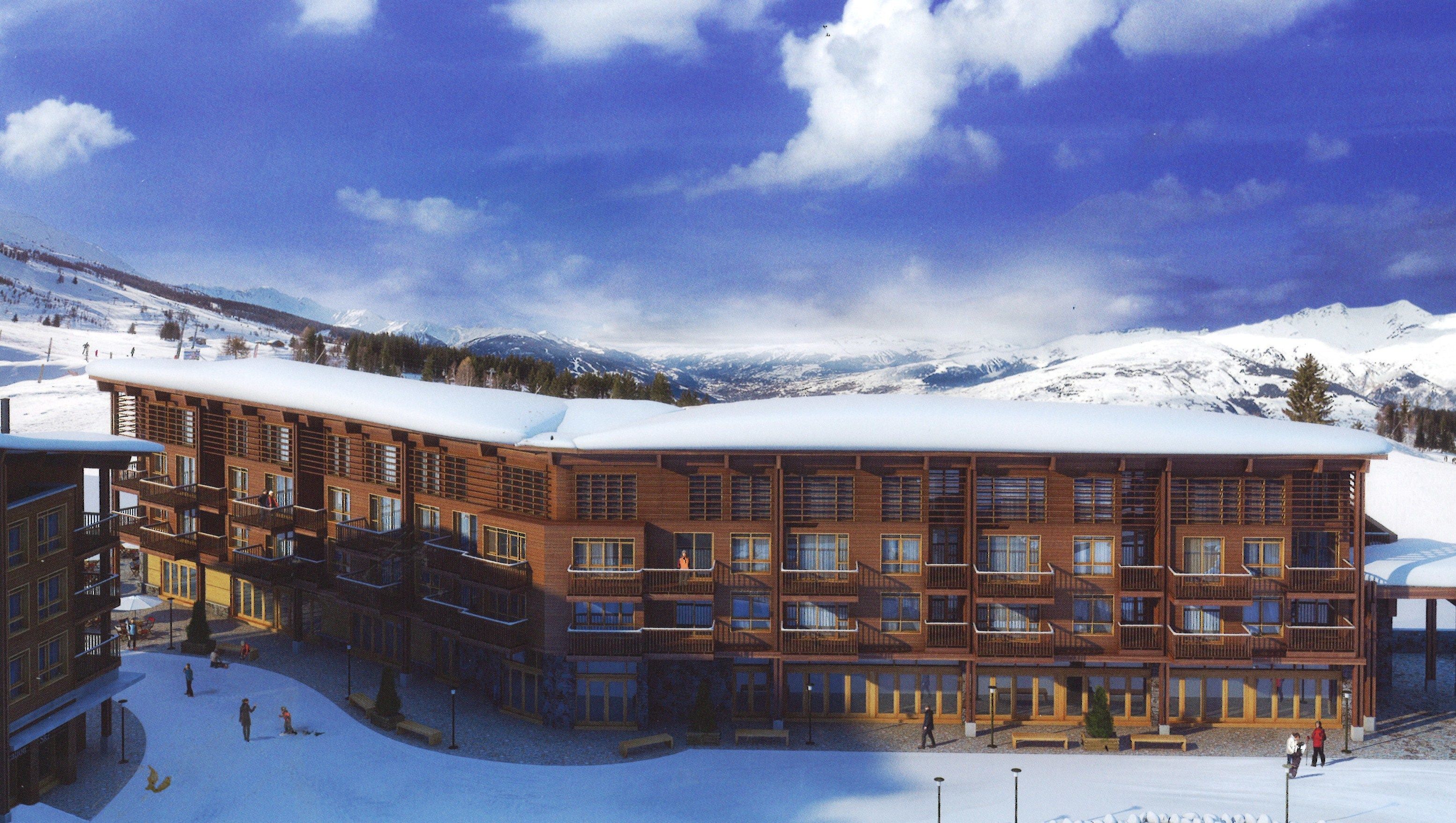 Un immeuble en bois à plusieurs étages, doté de balcons, entouré de montagnes enneigées.