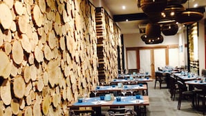 Un restaurante con una pared de troncos apilados, mesas con manteles azules y lámparas colgantes.