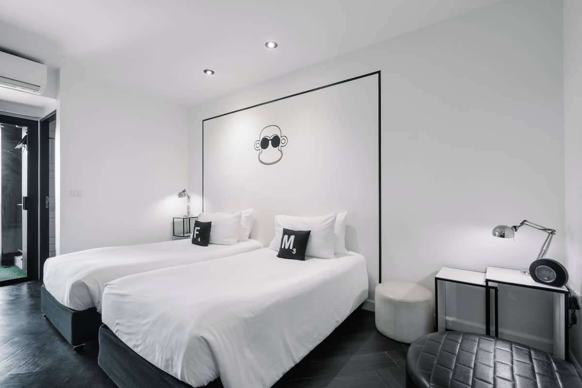 A modern hotel room with two beds, a desk, a chair, and a small stool.