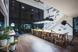 Un espacio de oficina moderno con una larga mesa de madera y sillas, una escalera y plantas en macetas.