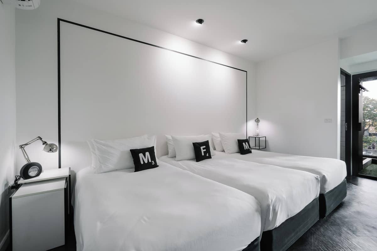 A modern hotel room with two beds, a desk with a lamp, and a large window.