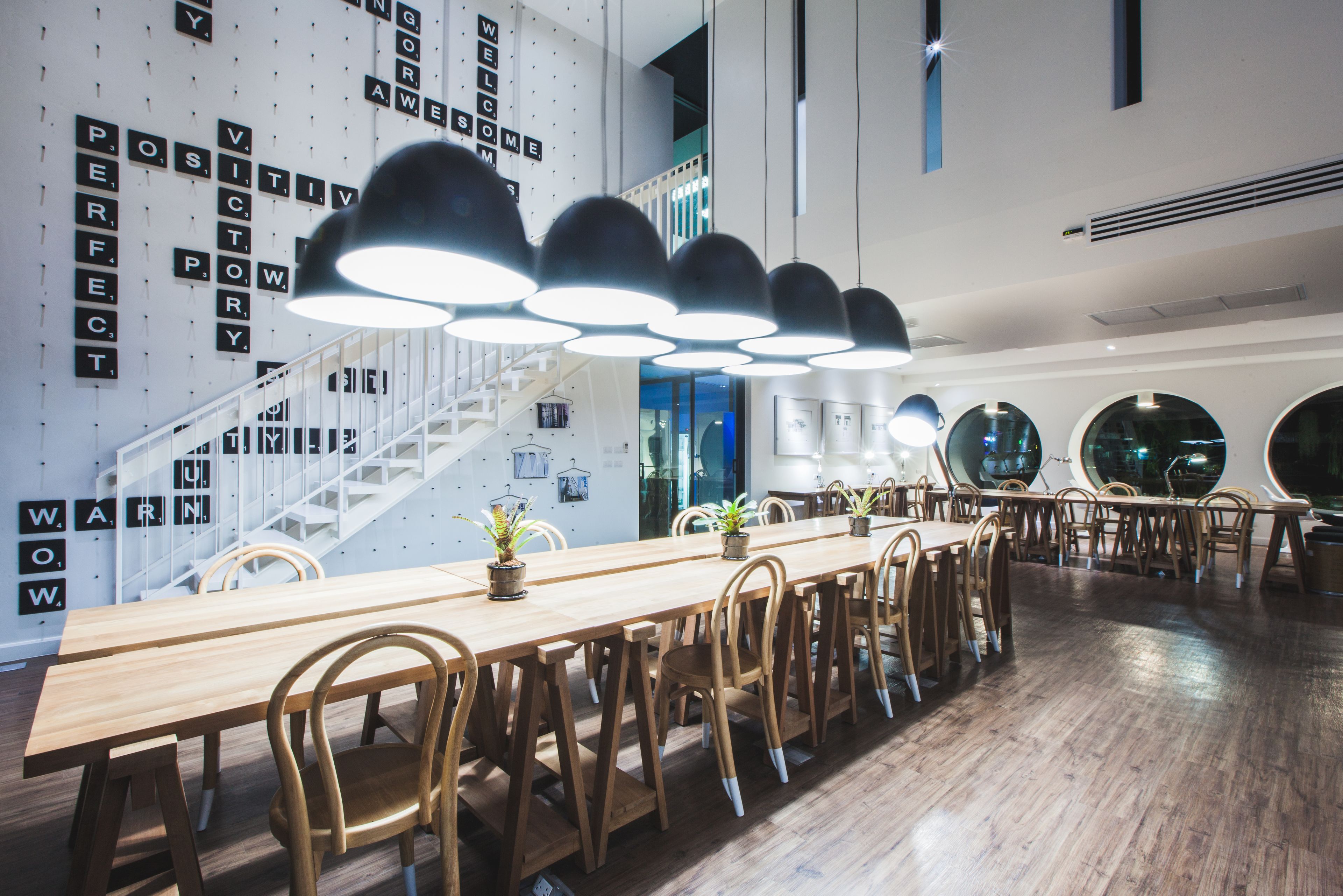 A modern dining area with a long wooden table, multiple chairs, and pendant lighting.