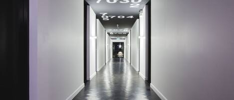 A long, narrow hallway with a dark floor and white walls. Numbers are displayed on the ceiling.