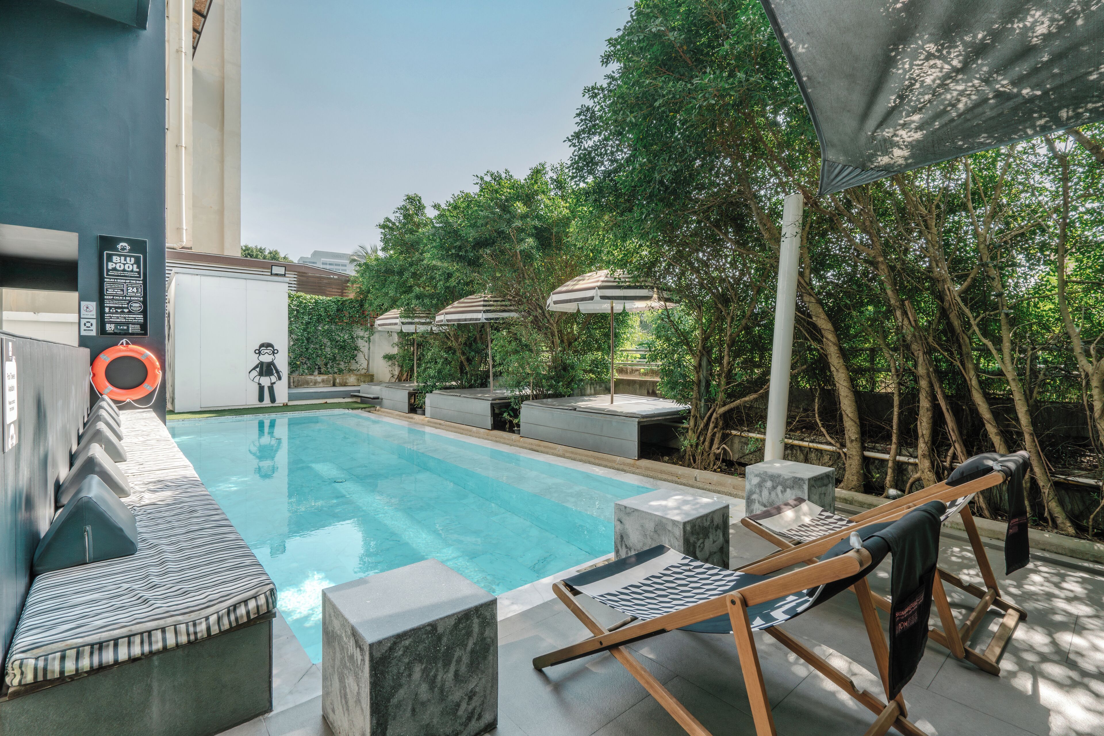 Une piscine entourée de verdure et d’un bâtiment moderne, avec des chaises longues et des parasols à proximité.