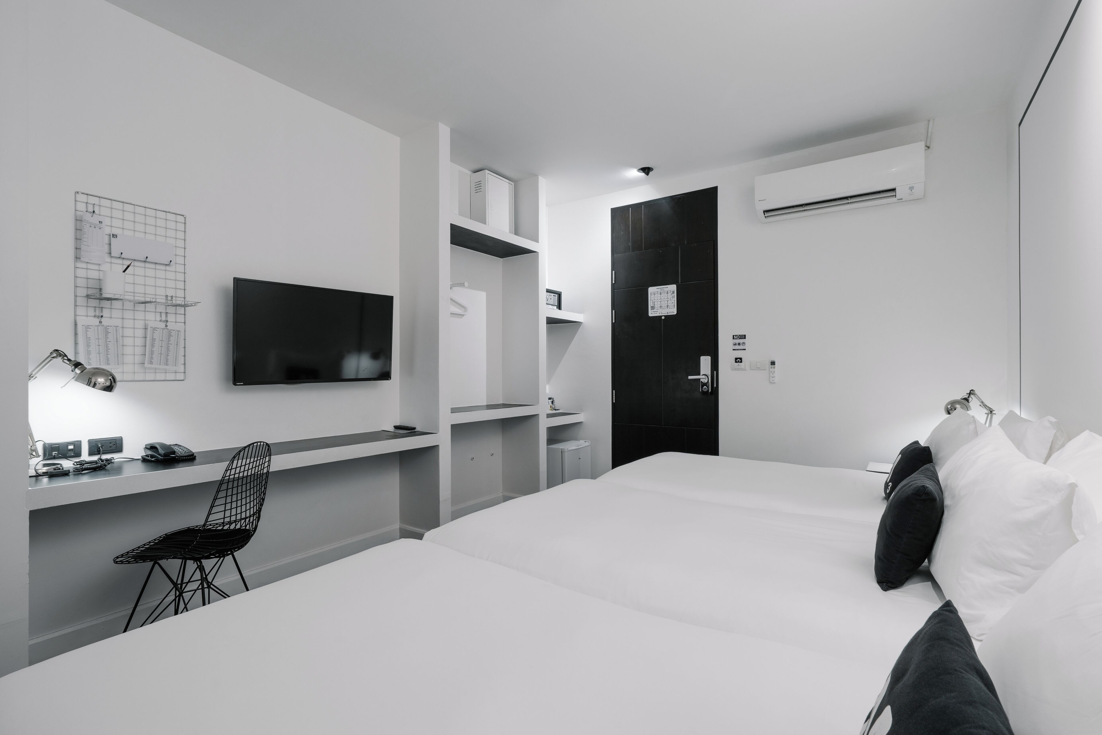 A modern hotel room with a large bed, a desk with a chair, a flat-screen TV, and an air conditioning unit.