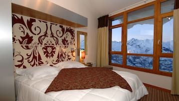 Ein Hotelzimmer mit einem großen Bett, einem dekorativen Kopfteil, einem Nachttisch mit Lampe und einem Fenster mit Bergblick.