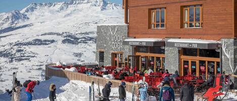 A ski resort with a restaurant and pub, outdoor seating, and a view of snow-covered mountains.