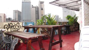 Una terrazza sul tetto con un tavolo e sedie in legno, piante in vaso e vista sullo skyline della città.