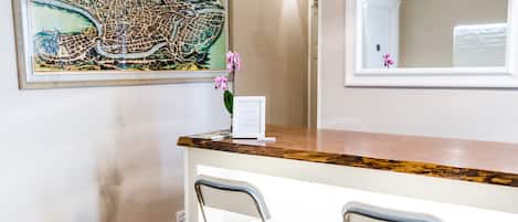 A room with a wooden floor, a white wall, a framed map, a mirror, and two metal chairs.