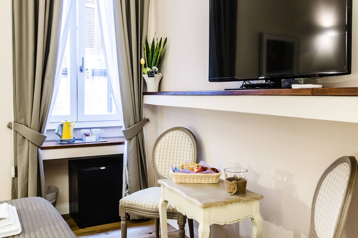 A hotel room with a bed, a desk with a computer, a television, and two chairs.