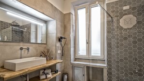 A modern bathroom with a large mirror, a rectangular sink, wooden shelves, a shower with a glass door, and hexagonal patterned walls. - Magenta Collection Sant'Anna (Rome)