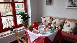 A dining area with a table set for two, a red and white tablecloth, and a window with a view of a bicycle and plants outside. - Hotel an de Marspoort (Xanten)