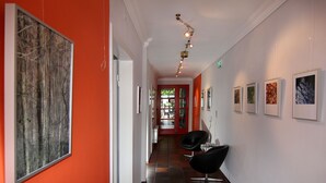 A hallway with artwork on the walls, a red door at the end, and two black chairs. - Hotel an de Marspoort (Xanten)