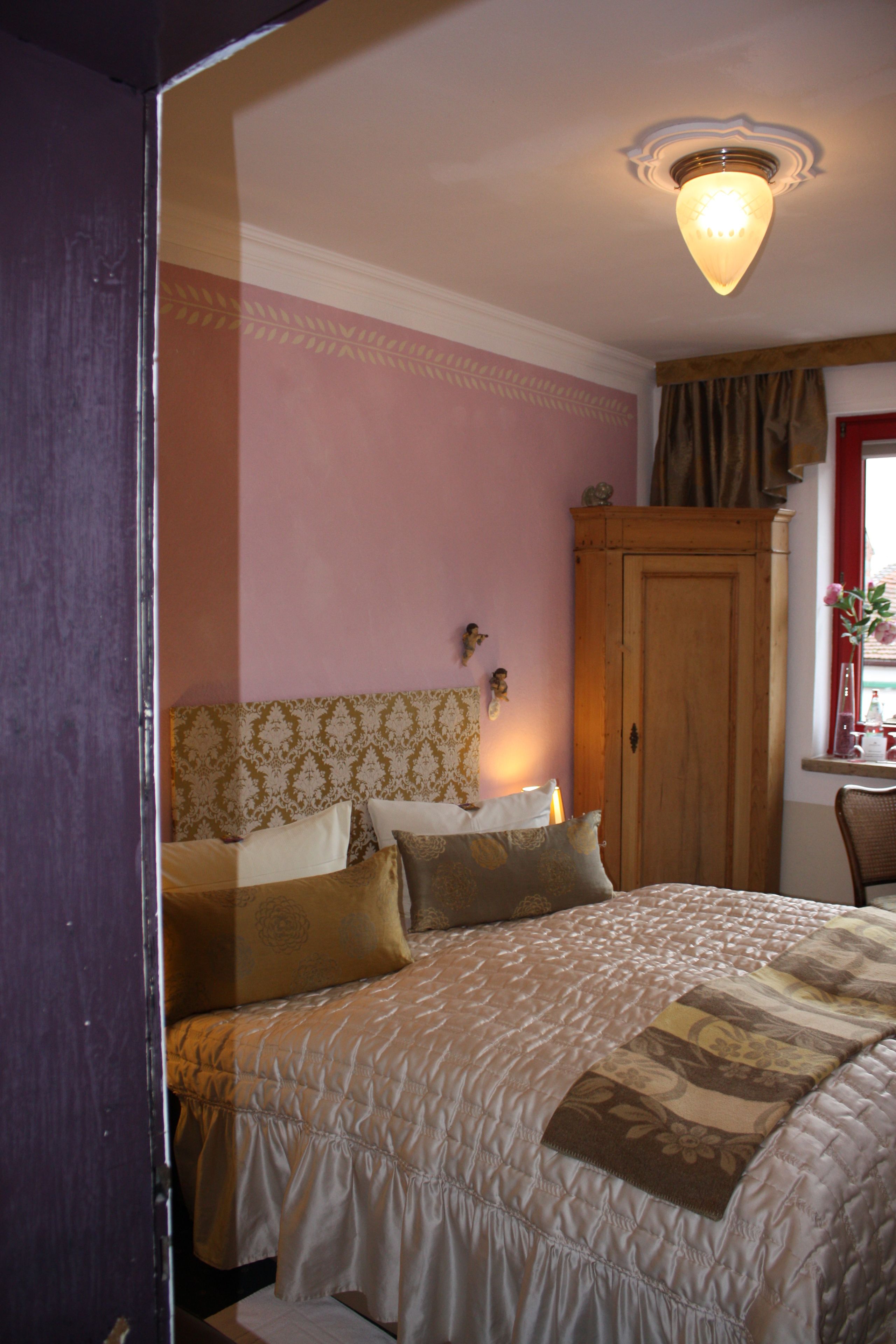 A bedroom with a bed, a wooden wardrobe, and a window with curtains.