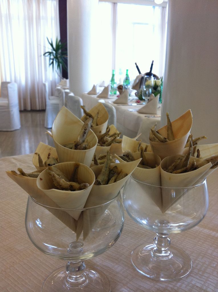 A table with several clear glass dishes containing food items, likely appetizers, in a well-lit indoor setting with a view of a window and a plant in the background.