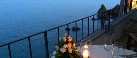 A table with a candle and glasses on a balcony overlooking the sea.