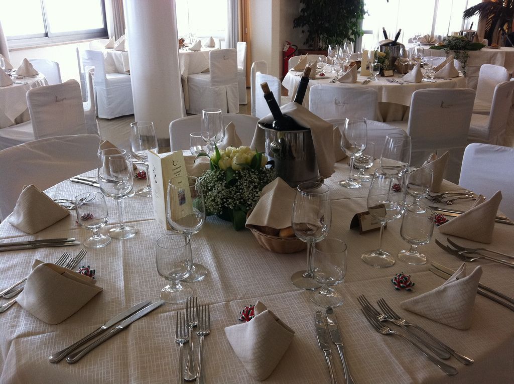 Een feestzaal met ronde tafels gedekt voor een formeel evenement, met witte tafelkleden, bestek en wijnkaraffen.