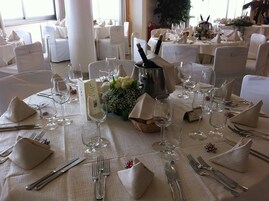 Un salón de banquetes con mesas redondas dispuestas para un evento formal, con manteles blancos, cubertería y copas de vino.