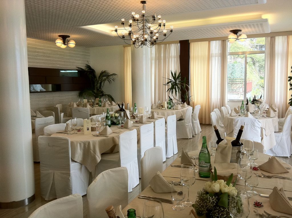 Une salle de banquet avec de nombreuses tables rondes dressées pour le repas, chacune étant recouverte d’une nappe blanche et agrémentée de chaises assorties.