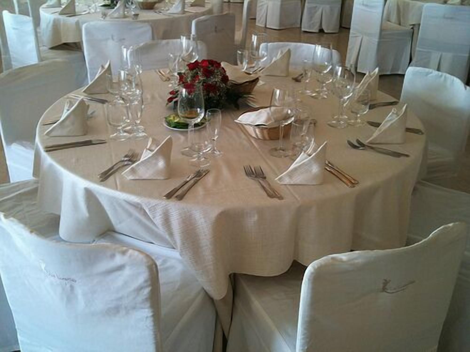 Une table ronde dressée pour un événement formel, avec des nappes blanches, des couverts en argent et de la verrerie élégante.