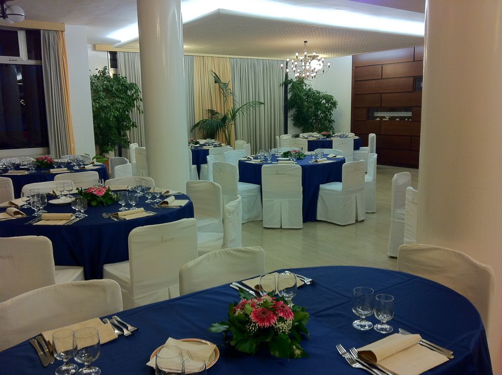 A banquet hall with round tables set for dining, white chairs, and blue tablecloths.