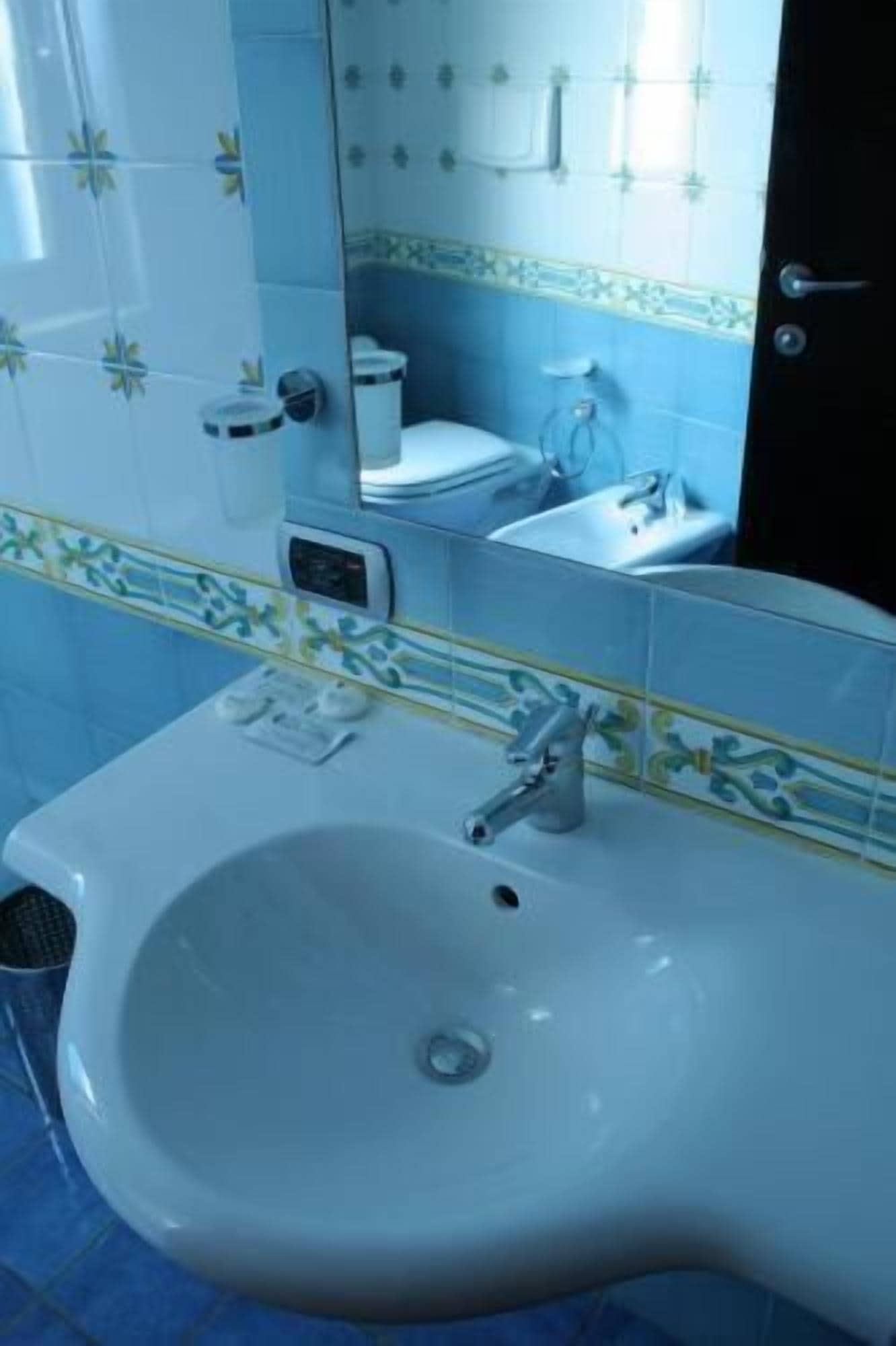 A bathroom with a white sink, a mirror, and blue-tiled walls.