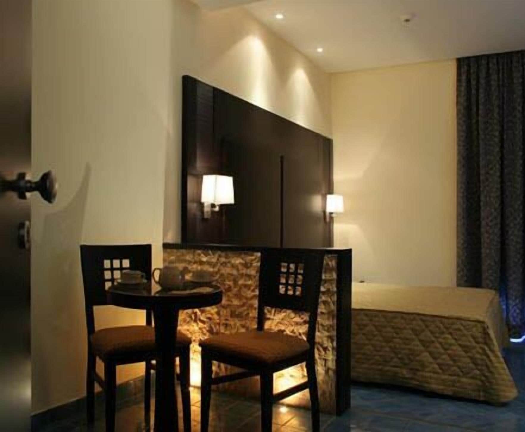 A hotel room with a bed, a small table with chairs, and two wall-mounted lamps.