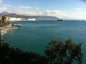 A coastal view with a large cruise ship docked at a pier, a beach, and a mountain in the background. - Hotel La Lucertola (Vietri sul Mare)