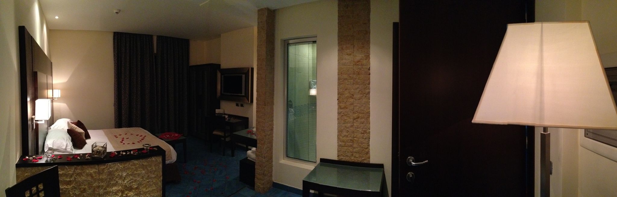 A hotel room with a bed, a desk, a TV, and a door.