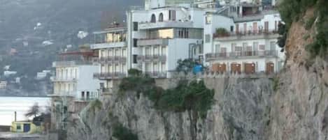 Un bâtiment situé sur la côte, doté de nombreux balcons et surplombant la mer, perché sur une falaise rocheuse.
