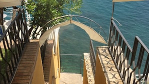 Una escalera conduce a un balcón con vista al mar, rodeado de paredes amarillas y barandillas de metal.