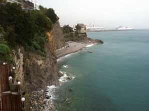 A coastal view with a rocky cliff, a beach, and a ship in the distance. - Hotel La Lucertola (Vietri sul Mare)