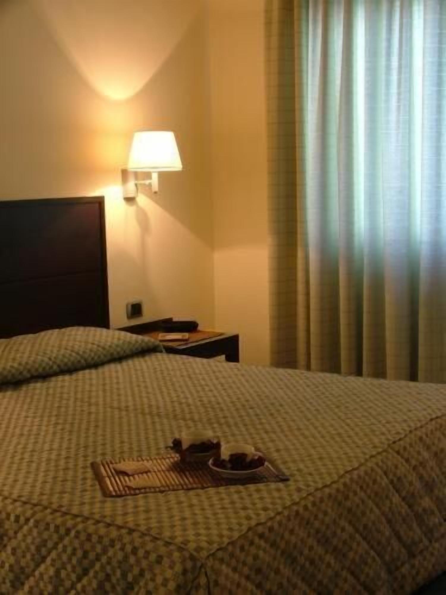 Une chambre d’hôtel avec un lit, une table de chevet, une lampe et une fenêtre avec des rideaux.