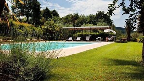 A swimming pool with lounge chairs and a covered seating area surrounded by greenery. - Campoli (San Casciano in Val di Pesa)