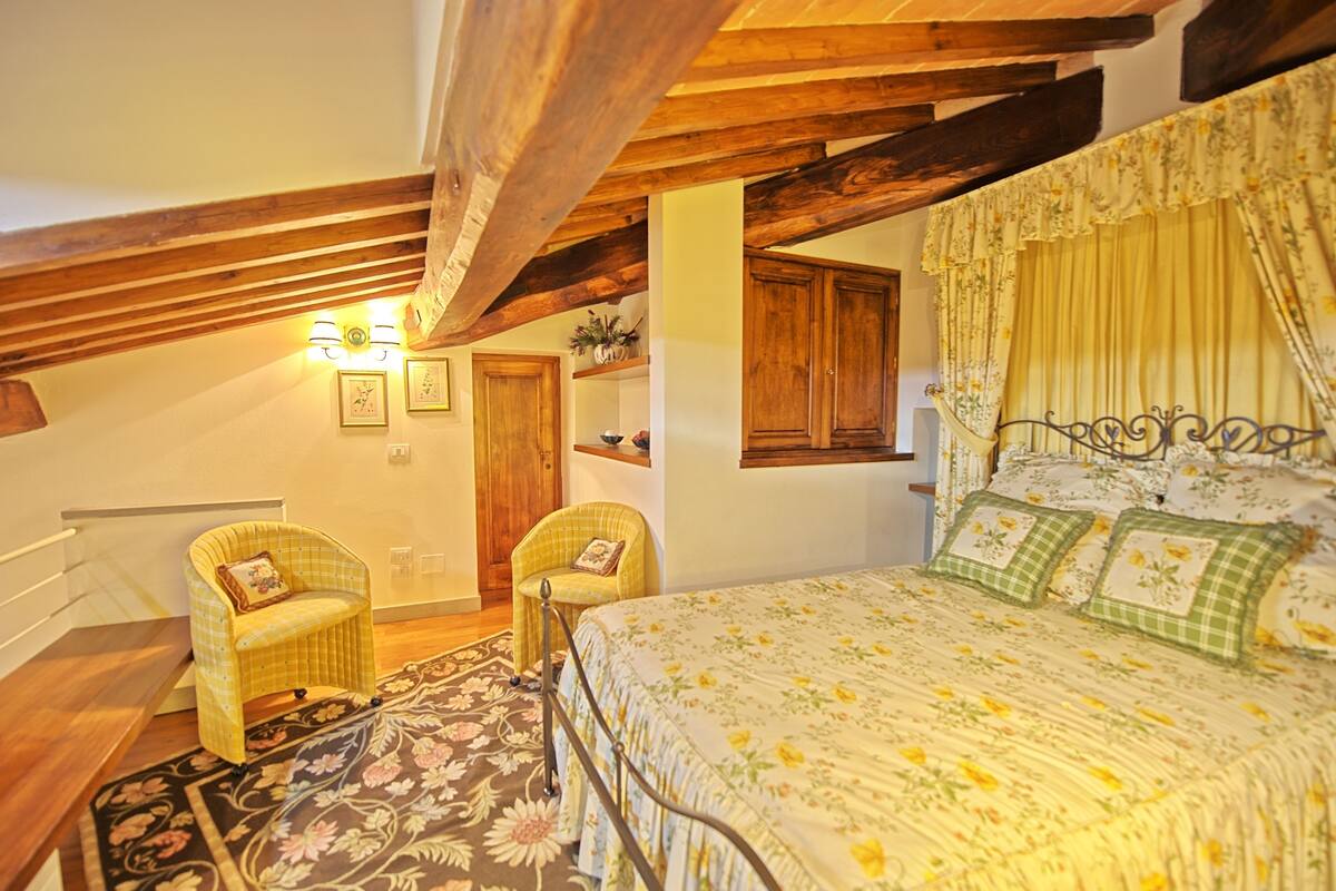 A bedroom with a bed, two chairs, a wooden ceiling, and a window with curtains.