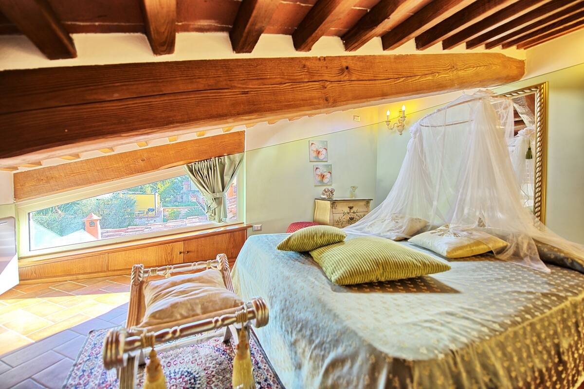 A bedroom with a large window, a bed with a canopy, and a wooden ceiling structure.