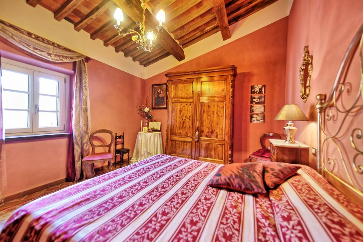 A bedroom with a wooden bed, a nightstand, a chair, a wardrobe, and a window with curtains.