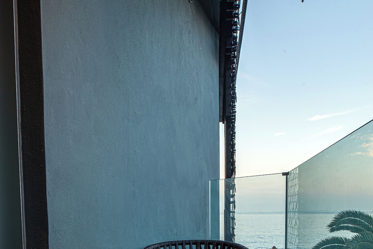 Un balcón con una mesa redonda y sillas de mimbre, con vistas al mar.