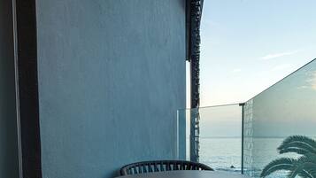 A balcony with wicker chairs and a table, overlooking the sea.