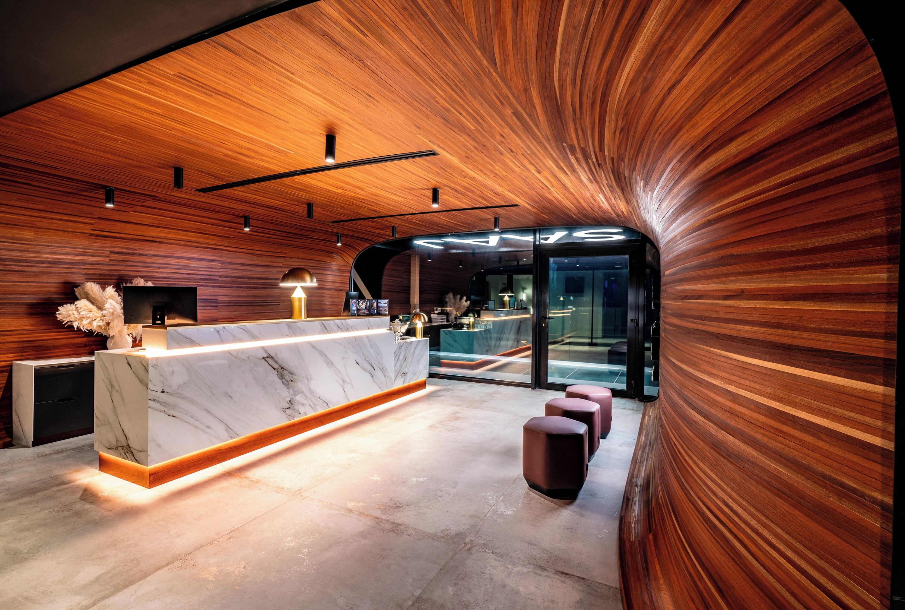Una moderna zona de recepción con mostrador de mármol, paneles de madera y techo curvo.