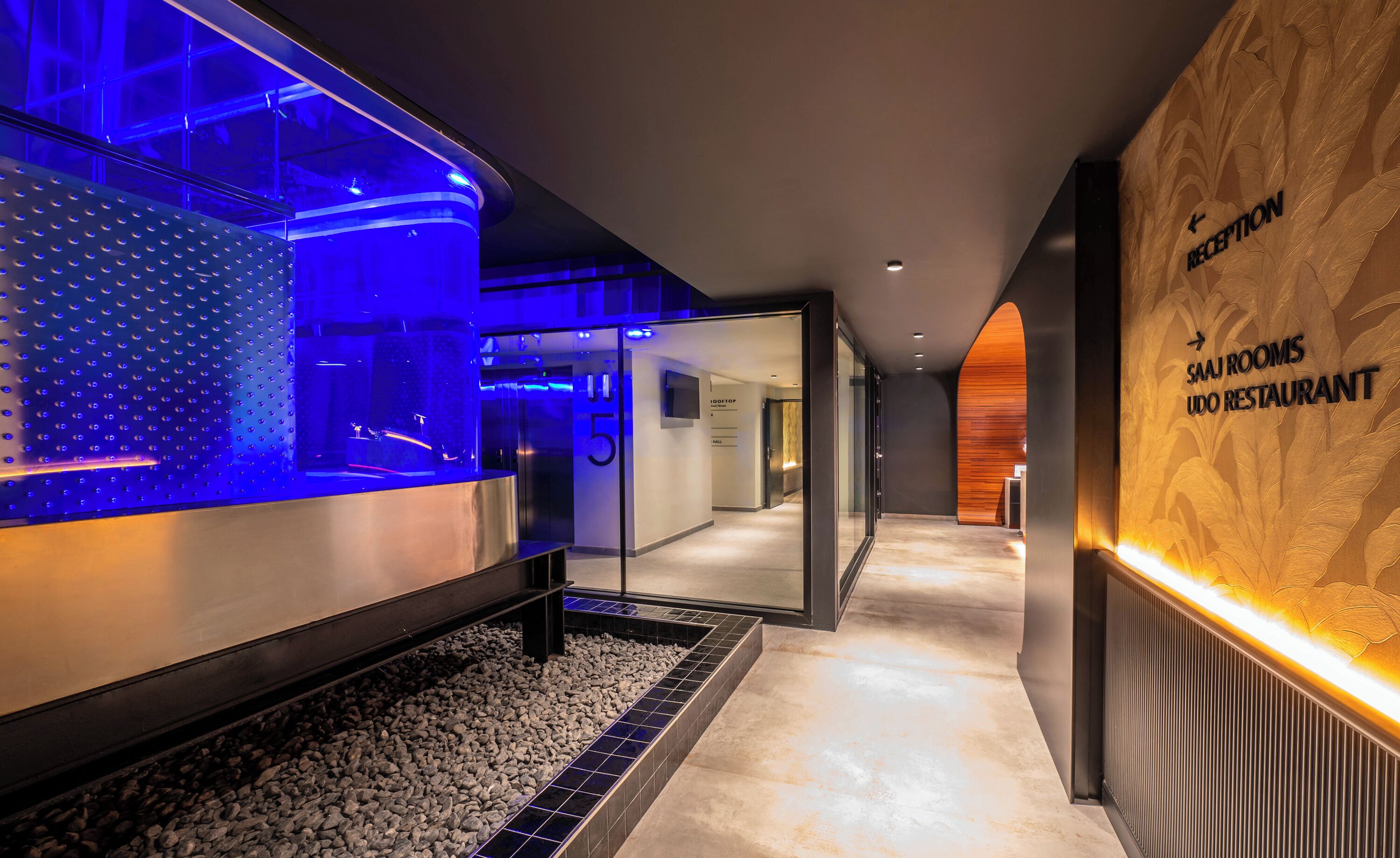 A modern hotel lobby with a reception desk, a reception area, and a sign for the Sam Room Udo Restaurant.