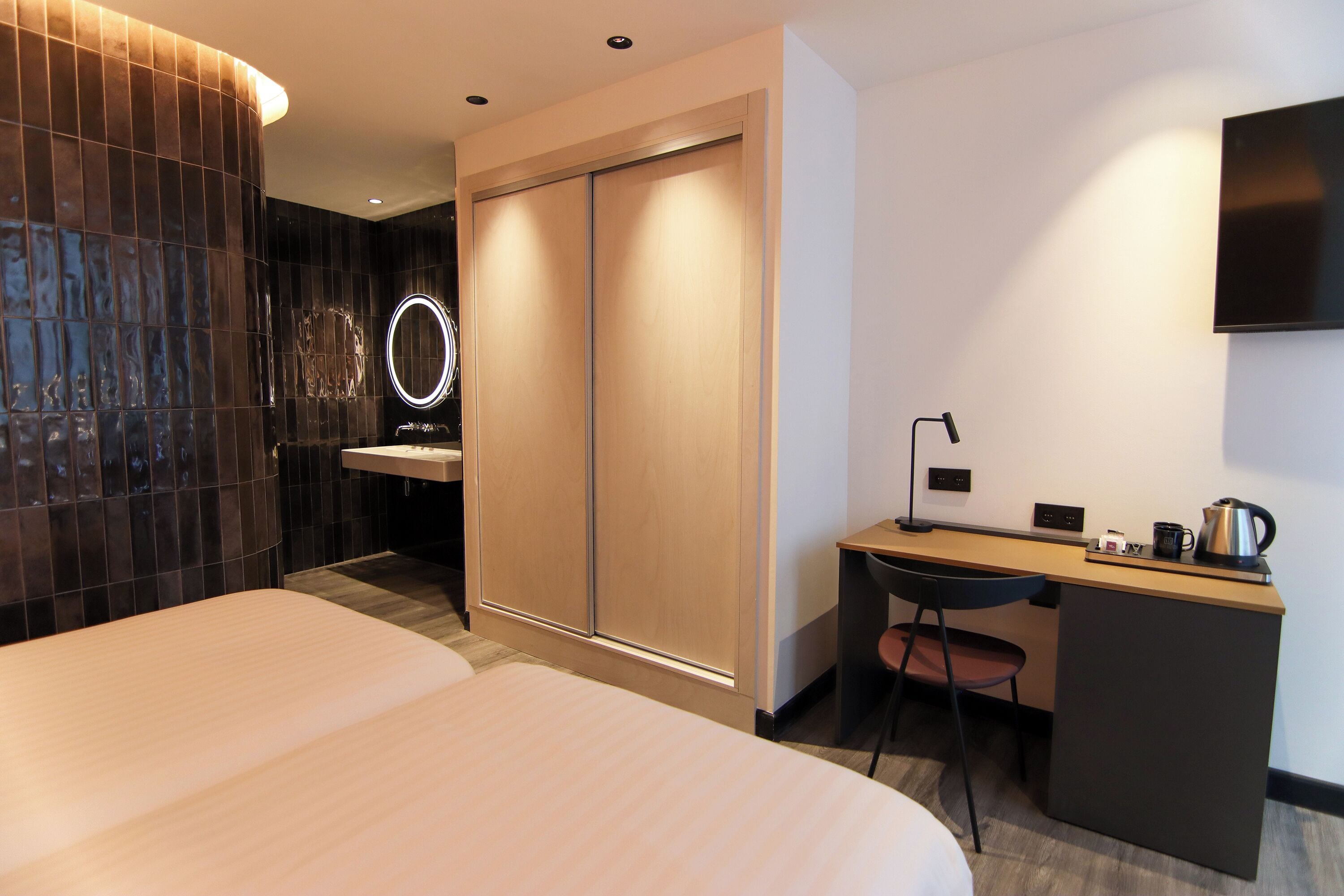 Ein modernes Hotelzimmer mit einem großen Bett, einem Schreibtisch, einem Sessel, einem Waschbecken und einem Fernseher.