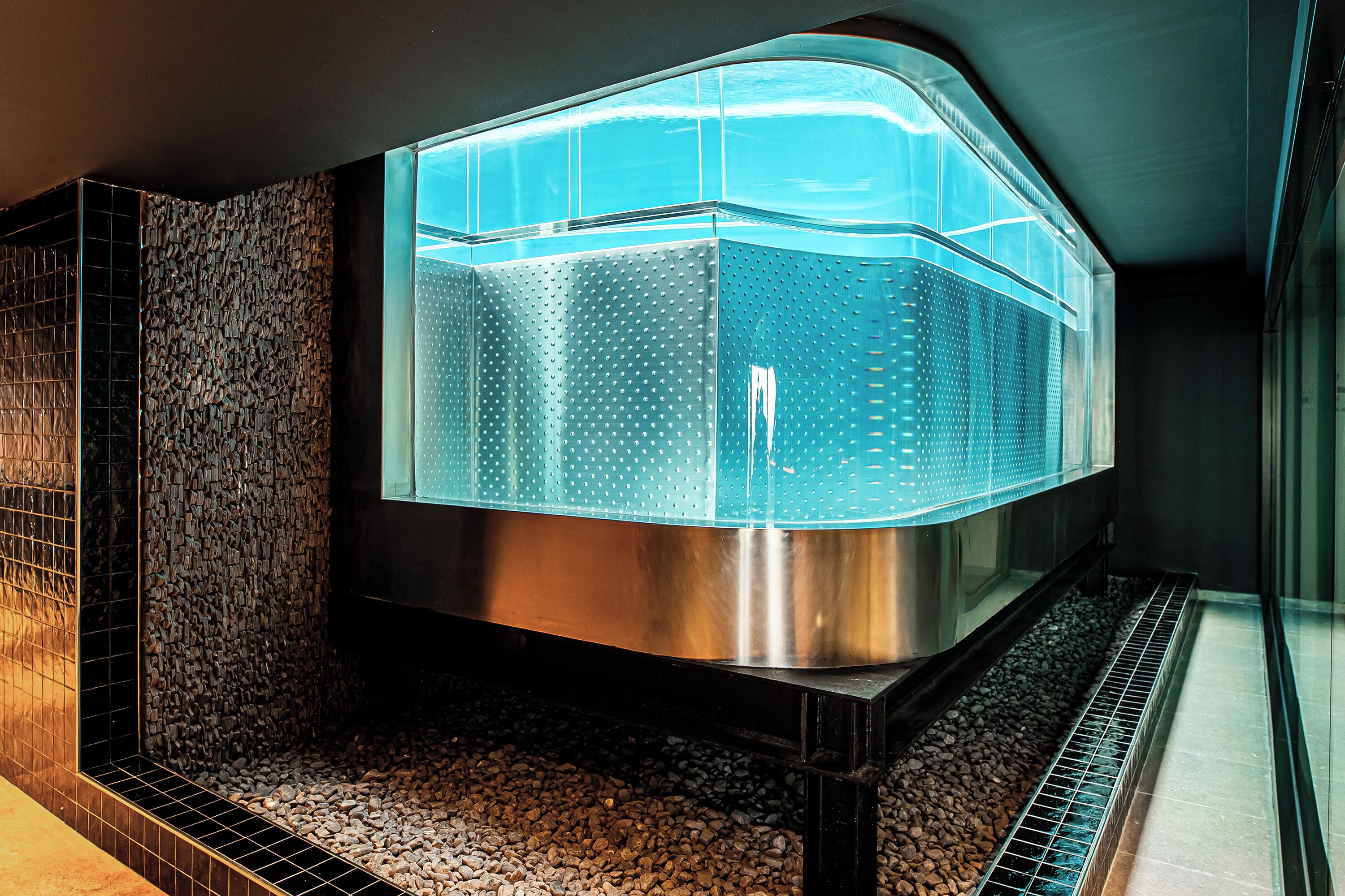 Een moderne spa-ruimte met een stenen muur, een metalen waterornament en een betegelde vloer.