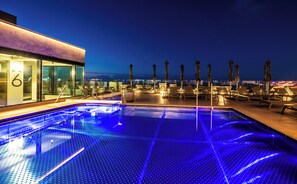 Una piscina al aire libre, sombrillas, sillones reclinables de piscina