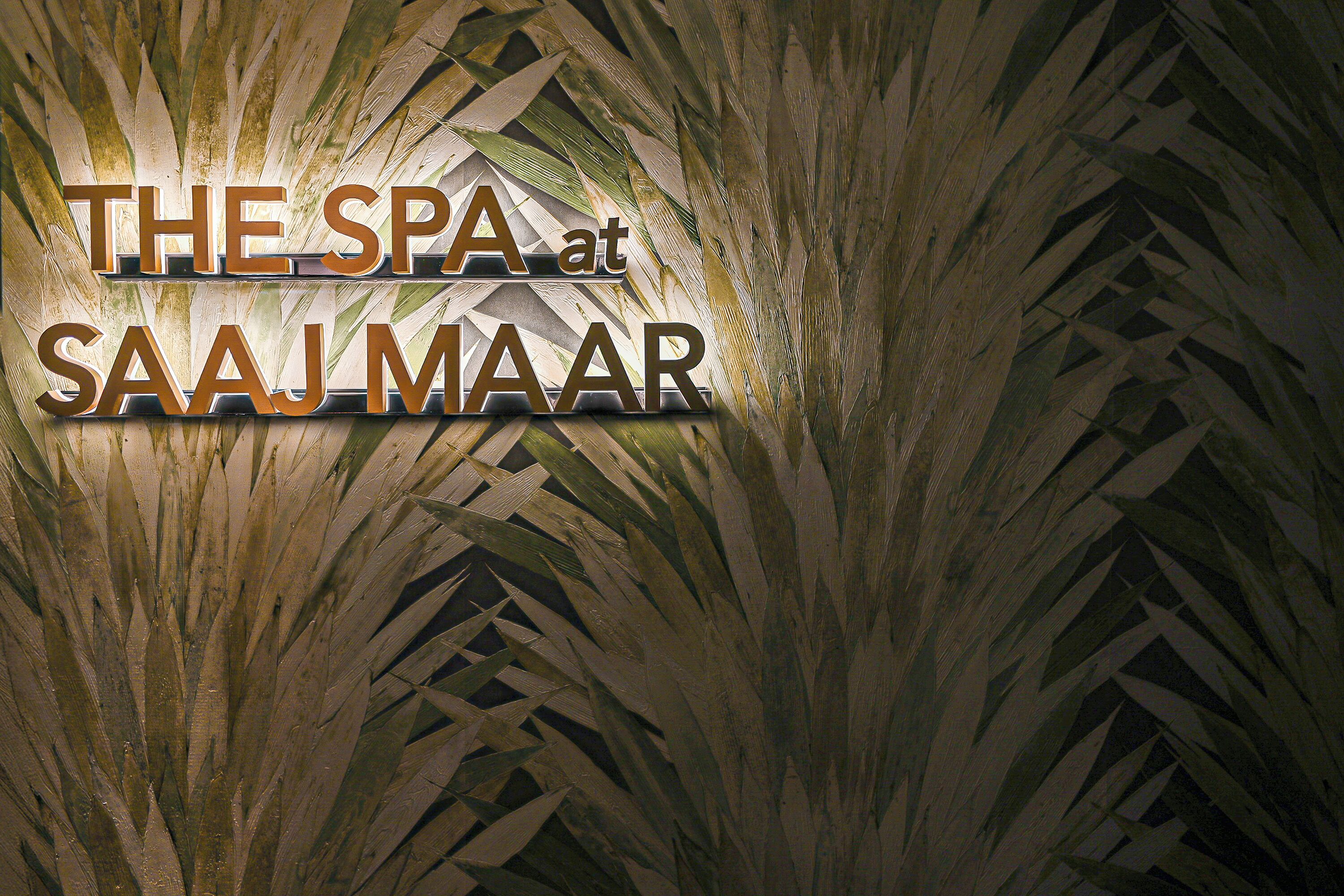 Un letrero con el texto 'THE SPA at SAJJ MAAR' sobre un fondo de hojas de palmera.