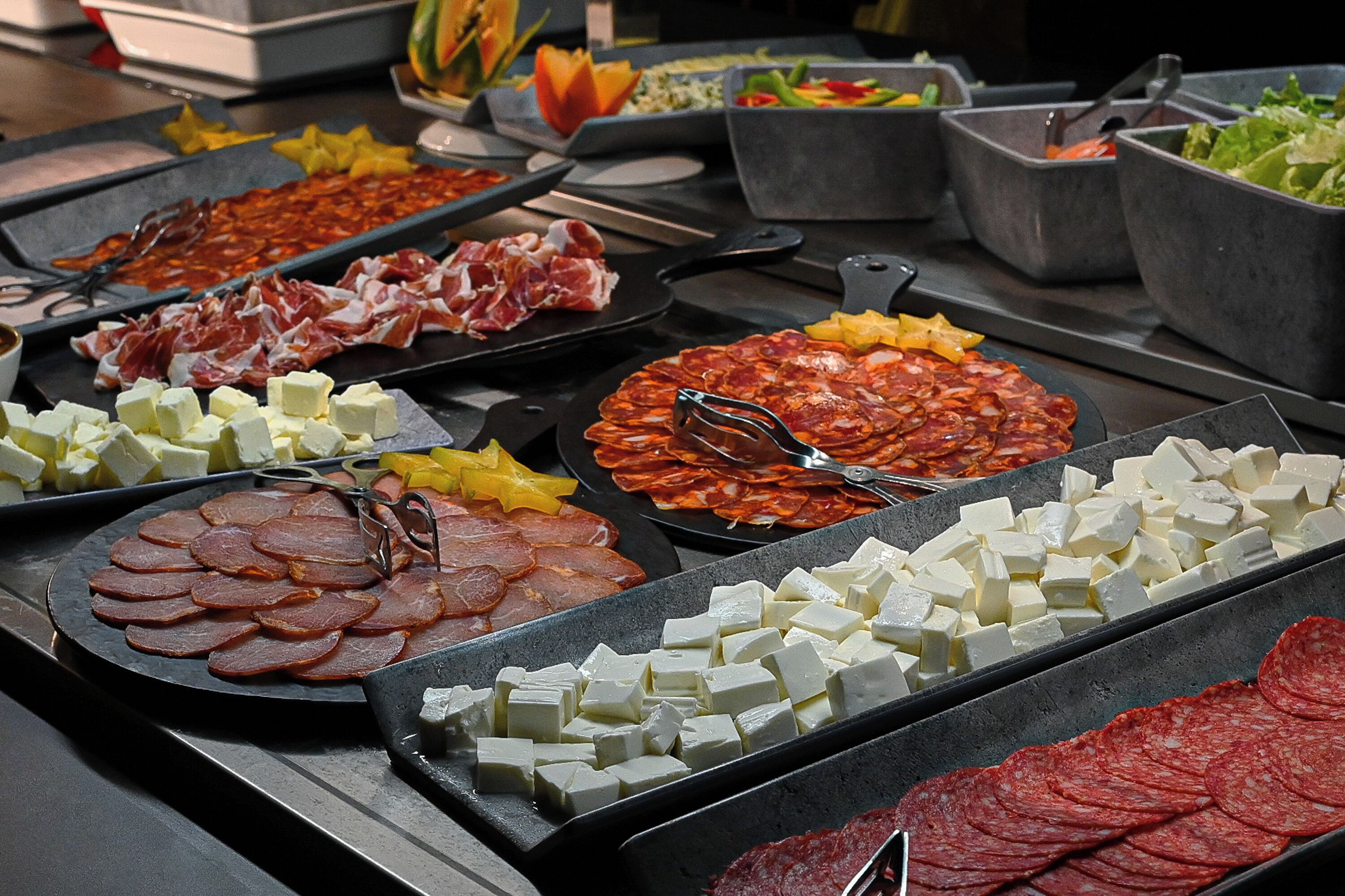 Ein Buffet mit verschiedenen Speisen, darunter Fleisch, Käse und Gemüse.